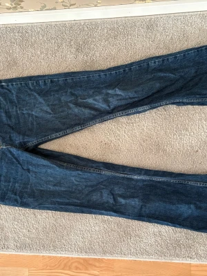 Mörkblå bootcut jeans - Säljer ett par mörkblå bootcut jeans med klassisk femficksdesign och lätt slitna detaljer. Jeansen har en rak passform upptill och utsvängda ben. Perfekta för dig som gillar en retroinspirerad look och vill ha ett par bekväma jeans i tidlös denim.
