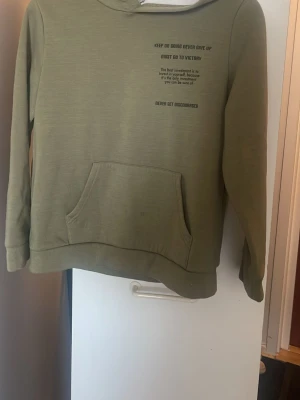 Olivgrön hoodie från Shein - Olivgrön hoodie från Shein med tryck på bröstet och stor magficka framtill. Insidan är fodrad med mjuk, vit fleece för extra komfort. Klassisk huva och avslappnad passform, perfekt för en chill och avslappnad stil. PRIS GÅR ATT DISKUTERAS! 