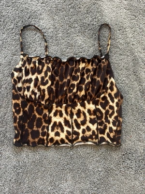 Leopardmönstrad croppad linnetopp - Snygg croppad linnetopp med leopardmönster och tunna axelband. Toppen har en figurnära passform och vågig kant nedtill. Perfekt för dig som vill sticka ut med ett djuriskt print.