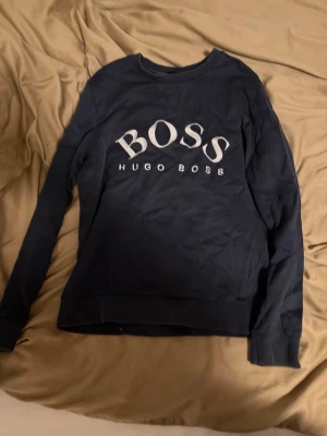 Mörkblå sweatshirt från Hugo Boss - Snygg mörkblå sweatshirt från Hugo Boss med stort vitt BOSS-tryck och logga på bröstet. Tröjan har rund halsringning och långa ärmar. Perfekt för en avslappnad och trendig stil.