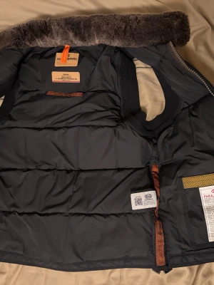 Svart dunväst från Parajumpers - Snygg svart dunväst från Parajumpers med hög krage fodrad i mjuk fuskpäls. Västen har två stora fickor med dragkedja och tryckknapp samt detaljer i orange. Perfekt för lager-på-lager och håller dig varm under kyliga dagar.