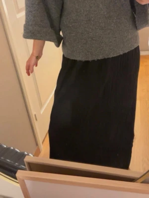 Svart långkjol i plisserad modell - Säljer en svart långkjol med plisserad struktur. Kjolen har en enkel och stilren design som passar till många olika looks. Resår i midjan för skön passform. Perfekt att matcha med en stickad tröja eller t-shirt.