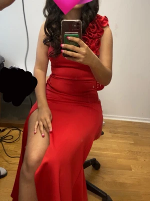 Röd oneshoulder långklänning - Snygg röd långklänning med oneshoulder och volangdetaljer på axeln. Klänningen har en hög slits på sidan och figurnära passform. Perfekt för dig som vill sticka ut med en elegant och trendig look.