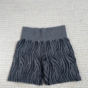 Grå zebramönstrade cykelshorts - Säljer ett par grå träningsshorts från NVGTN med svart zebramönster och bred ribbad midja. Endast använda 1 gång av mig så mycket bra skick!
