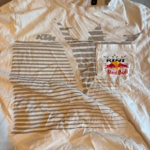 Vit KTM Red Bull t-shirt - Säljer en vit t-shirt från KTM Red Bull med gråa ränder och logotyp på bröstfickan. Dock ett litet hål på ena axeln 