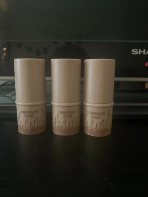 Tre helt oanvända concealer stick blush, bronser, blush - Tre concealer sticks i beige plast med brunt grafiskt mönster längst ner. Cylindrisk form och praktisk storlek som är enkel att ta med. Perfekt för att täcka mörka ringar och små blemmor. Helt oanvända köpte för 100kr styck.