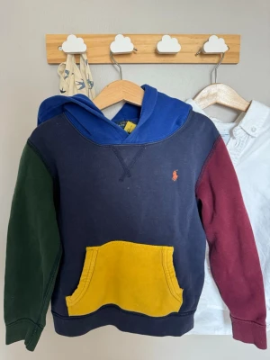 Färgglad hoodie från Polo Ralph Lauren - Snygg hoodie i flera färger från Polo Ralph Lauren. Marinblå bas med blå huva, grönt och vinrött på ärmarna samt en gul magficka. Klassisk logga broderad på bröstet. Tillverkad i mjuk bomull, perfekt för en avslappnad och cool stil.