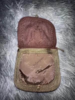 Vintage plånbok från Yves Saint Laurent - Snygg vintage plånbok från Yves Saint Laurent i brunt tyg med guldfärgade broderade detaljer. Plånboken har en unik form med lock och dragkedja, samt YSL-logga på insidan. Perfekt för dig som gillar klassisk och elegant design.