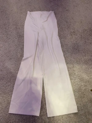 Vita utsvängda leggings med hög midja - Säljer ett par vita leggings med hög midja och utsvängda ben. De är stretchiga och sitter tajt upptill men blir vidare nedtill. Perfekta för dig som gillar en clean och trendig look. Materialet känns mjukt och följsamt.
