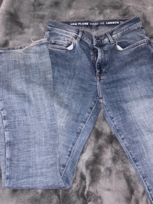 Blå low flare jeans XS - Snygga blå low flare jeans i storlek XS. Jeansen har klassisk femficksdesign, låg midja och lätt tvättad look. Perfekta för dig som gillar en avslappnad men trendig stil. Tillverkade i mjukt denimtyg.