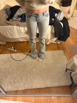 Ljusblå  bootcut jeans - Säljer ett par ljusblå bootcut jeans med slitningar och hål vid knäna. Jeansen har klassisk femficksdesign och är tillverkade i denim med en skön stretch. Perfekta för en avslappnad och trendig look.
