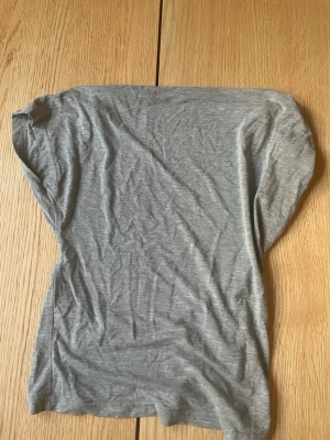 Grå kortärmad topp i bomull - En enkel och mjuk grå topp med korta ärmar och rund hals. Tillverkad i tunt bomullsmaterial som känns skönt mot huden. Perfekt att styla med jeans eller kjol för en avslappnad look.