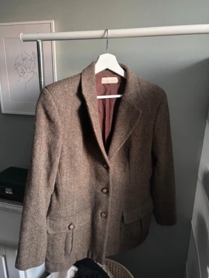 Brun tweedkavaj i irländskt ull - Vintage brun tweedkavaj med två framfickor och knappar. Kavajen har en skräddad  passform, spetsiga slag och är helfodrad i brunt tyg. Perfekt för dig som gillar tidlös och stilren look.