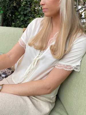Sidenblus med spetsdetaljer  - Så fin blus i en mjuk vit/cremefärg med vackra spetsdetaljer. Perfekt för en romantisk och somrig look 