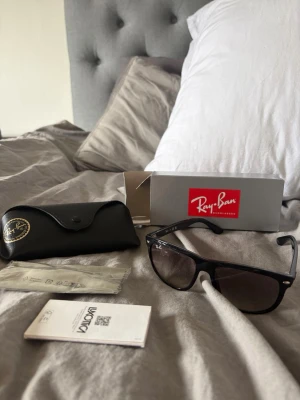 Svarta Ray-Ban Wayfarer solglasögon - Klassiska svarta Ray-Ban Wayfarer solglasögon helt nya oanvända , med bred båge och mörka glas. Säljes med originalfodral, putsduk och box. Perfekt accessoar för dig som vill ha en tidlös och ikonisk look.
