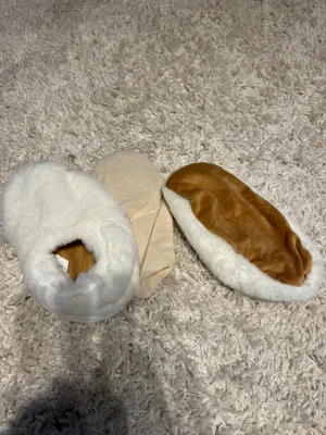 Vita och bruna fluffiga tofflor - VÄRMETOFFLOR😍Mysiga tofflor i vitt och ljusbrunt med fluffig utsida och mjuk insida. Tofflorna har en enkel slip-in modell och är tillverkade i syntetmaterial som känns riktigt skönt mot fötterna. Perfekta för att hålla värmen hemma under kalla dagar. Aldrig använda. Står ej storlek men skulle tippa på 38-39. 