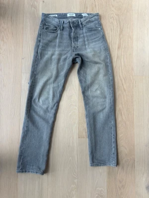 Grå raka jeans från Jack and Jones - Säljer ett par grå jeans från Jack and Jones med rak passform och klassisk femficksdesign. Jeansen har normal midja. Perfekta för en clean och avslappnad stil.