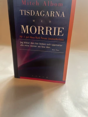 Tisdagarna med Morrie av Mitch Albom - En inbunden bok med titeln 'Tisdagarna med Morrie' av Mitch Albom. Omslaget är blått med röda och vita detaljer och text. Boken är på svenska och har ett klassiskt, stilrent utseende. Perfekt för dig som gillar gripande och tänkvärd skönlitteratur.