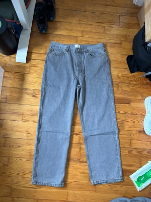 Grå raka jeans från Aimé Leon Dore - Säljer ett par grå jeans från Aimé Leon Dore i rak modell. Jeansen har klassisk femficksdesign, knappgylf och är tillverkade i slitstark denim. Perfekta för en clean och avslappnad stil.