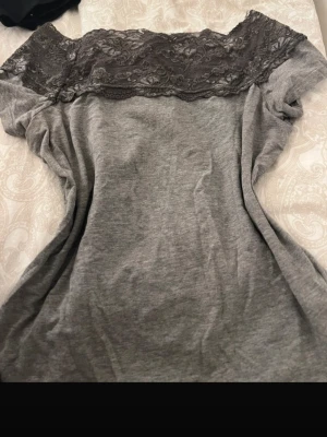 Grå nattlinne med spets upptill - Mysigt grått nattlinne med bred spets upptill över axlar och byst. Tillverkat i mjukt material som känns skönt mot huden. Avslappnad passform och enkel design med en feminin touch tack vare spetsdetaljen.