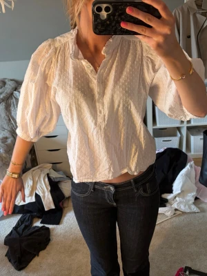 Vit blus med puffärm och struktur - Säljer en vit blus med puffiga trekvartsärmar och diskret strukturmönster. Blusen har knappar framtill och en avslappnad passform. Perfekt till jeans eller kjol för en trendig look.