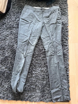 Gråa kostymbyxor i linneblandning - Snygga grå kostymbyxor med smal passform och pressveck. Byxorna har bälteshällor, knapp och dragkedja fram. Tillverkade i ett tunt, svalt tyg som känns som linne. Perfekta för en clean och stilren look.