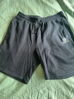 Svarta shorts från Converse med snörning - Snygga marinblå herrshorts från Converse med elastisk midja och snörning framtill. Tillverkade i mjuk bomull och har fickor på sidorna samt en bakficka. Perfekta för sommardagar eller chill hemma.