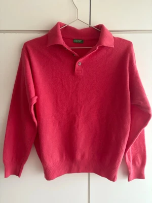  Stickad tröja från Benetton 100% wool  - Snygg rosa/röd stickad tröja från United Colors of Benetton med klassisk krage och knappdetalj vid halsen. Tröjan har långa ärmar och ribbade muddar vid ärmslut och nederkant. Perfekt för dig som gillar färg och en 2000s stil. Denna tröja är också 100% cahmire och köptes från Italien för ca 1000 kr. Pris kan diskuteras 🥰