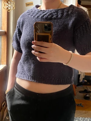 Mörkblå stickad kortärmad tröja - Säljer en mörkblå stickad tröja med korta ärmar och rund halsringning med flätmönster. Tröjan är croppad och har ribbstickade detaljer vid ärmslut och nederkant. Ganska tjockt material. 