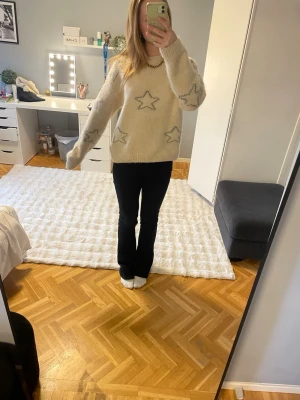 Beige stickad tröja med stjärnor - Mysig beige stickad tröja med grå stjärnmönster över hela tröjan. Tröjan har en avslappnad passform, rund halsringning och långa ärmar. Perfekt för dig som gillar en chill och trendig stil.