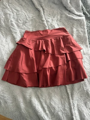 Röd volangkjol med lager - Supersöt röd kortkjol med flera volanglager som ger en riktigt flowy känsla. Kjolen har bred linning och är perfekt för dig som vill ha en lekfull och trendig look. Tillverkad i mjukt tyg som känns skönt mot huden.