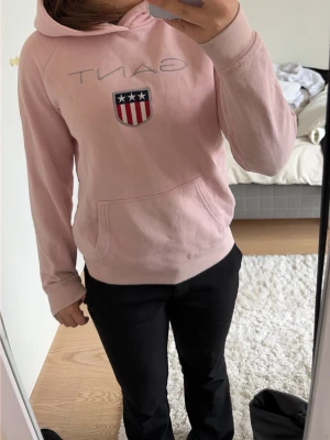 Ljusrosa hoodie från GANT - Säljer en ljusrosa hoodie från GANT med broderad logga och amerikanskinspirerat sköldmärke på bröstet. Hoodien har en stor känguruficka framtill och klassisk huva. Perfekt för en avslappnad och stilren look. Hoddien har några märken som inte går bort, men de syns knappt inte - därav det låga priset.