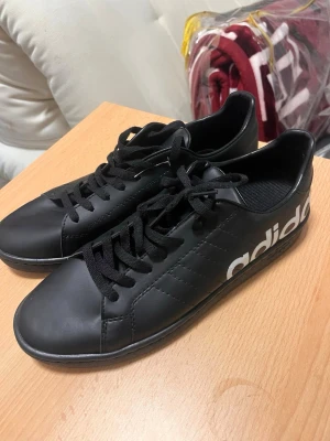 sneakers  - Snygga svarta sneakers från Adidas med stor vit logga på sidan. Skorna har klassisk låg profil, svarta skosnören och ovandel i slätt syntetmaterial. Perfekta för dig som gillar stilrena och sportiga skor.