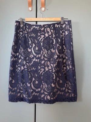 Mörkblå spetskjol från In Wear - Säljer en elegant mörkblå kjol från In Wear med vacker spets och blommigt mönster. Kjolen är kort (en dm ovanför knä på mig som är 168cm) och har en beige underkjol som ger en snygg kontrast till spetsen. Perfekt för dig som vill ha en feminin och stilren look.