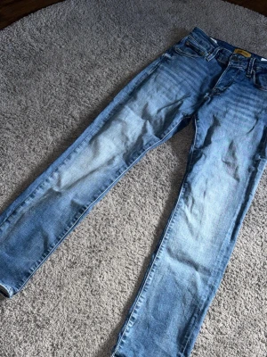 Ljusblå jack & Jones  jeans - Säljer ett par ljusblå jack & Jones  jeans med raka ben och klassisk femficksdesign. Jeansen har en snygg tvättad look och är tillverkade i denim. Perfekta för en avslappnad och trendig stil.
