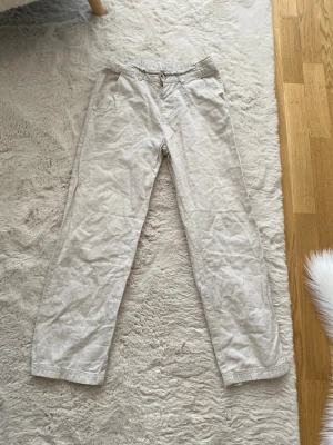 Beiga linnebyxor med resårmidja - Snygga beiga linnebyxor från KappAhl med avslappnad passform, resår i midjan och knappstängning. Byxorna har sidofickor och bälteshällor, perfekta för en chill och stilren look. Tillverkade i ett luftigt linnematerial som passar perfekt till sommaren.