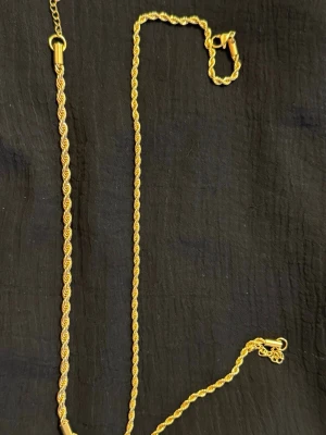 Guldpläterad halsband och armband  - Snyggt halsband och armband i guldfärg med tvinnad kedja och klassisk karbinhake. Smyckerna har en elegant och stilren design utan hänge eller extra detaljer. Perfekt för dig som gillar minimalistiska smycken med lite extra glans. En jättefin guldpläterad set för en bra pris!