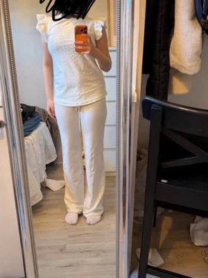 Vit topp med volangärmar - Söt vit topp med broderade detaljer och volangärmar. Toppen har rund halsringning och är gjord i ett lätt, luftigt material som känns fräscht. Perfekt att styla med jeans eller kjol för en trendig look.