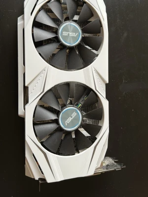 ASUS vit grafikkort med dubbla fläktar, 10/10 kvalitet - Snyggt vitt grafikkort från ASUS med två stora svarta fläktar och stilrena detaljer. Kortet har en robust design med ASUS-logga på sidan och passar perfekt för gaming eller krävande datoranvändning. Materialet är mestadels plast och metall.