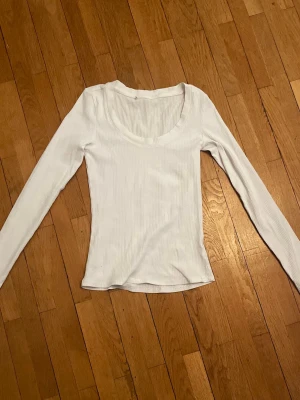 Vit ribbad långärmad topp - En enkel och stilren vit ribbad topp med lång ärm och rundad halsringning. Perfekt att matcha med jeans eller kjol för en clean look. Materialet är mjukt och stretchigt för en bekväm passform.
