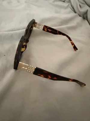 Bruna rektangulära solglasögon - Snygga solglasögon med rektangulära bågar i brunmelerat mönster och guldfärgade detaljer vid skalmarna. Glasen är mörka och bågarna har en trendig, chunky look. Perfekta för dig som vill sticka ut med accessoarerna.