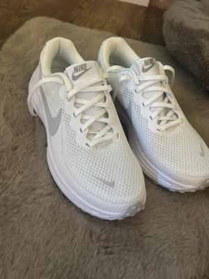 Vita Nike sneakers med mesh - Snygga vita Nike sneakers med lågt skaft och klassisk silhuett. Ovandelen är i ventilerande meshmaterial och har vita skosnören samt en ljusgrå Nike Swoosh på sidan. Sulan är vit och ger en sportig look. Perfekta för dig som gillar stilrena och bekväma skor. Endast testade