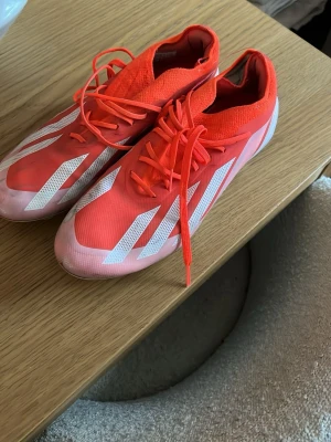 Adidas crazyfast elite  - Säljer ett par röda adidas crazyfast elite från Adidas med vita ränder på sidorna. Skorna har snörning och en strumpliknande ovandel i textil för skön passform. Yttermaterialet är syntet och designen är slimmad för bra bollkontroll på planen. Lite slitningar inuti båda skorna men inget som gör skillnad på planen.