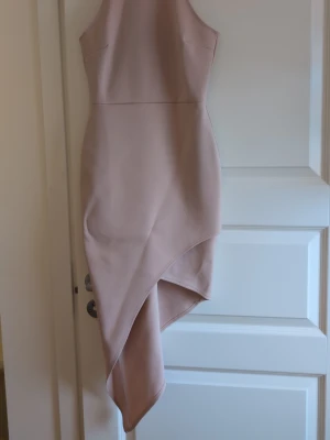 Ljus asymmetrisk omlottklänning NLY One - Säljer en ljusrosa, nude, asymmetrisk omlottklänning från NLY One i storlek S. Klänningen är tillverkad i mjuk polyester med stretchig elastan och har en elegant wrap-design som ger en snygg siluett. Perfekt för dig som gillar stilrena och trendiga plagg.