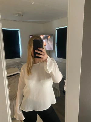 Vit blus med volangärm från Only - Säljer en stilren vit blus från Only med rund halsringning och långa, lätt utsvängda ärmar med volangkant. Blusen har en flowy passform och är tillverkad i ett tunt, lätt material som ger ett elegant intryck.