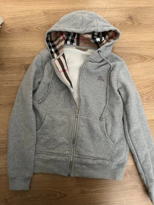 Grå zip hoodie - Snygg grå hoodie med dragkedja och rutig mönster innanför som ger den en unik look. Bra passform och storlek S. Super bekväm, mjuk och varm. Har knappt använts och är i väldigt gott skick med inga tecken på bruk. Skicka om du är intresserad! Svarar gärna på frågor och är öppen till bud! Klädetiketten är bortklippt men har fortfarande kvar den.