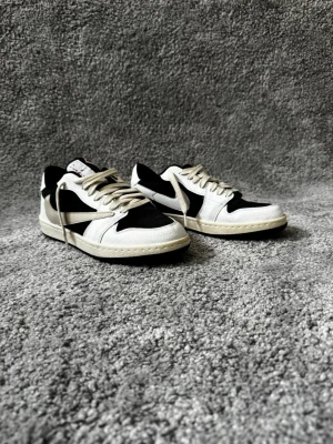 Nike svartvita sneakers med mockadetaljer - Säljer ett par stilrena svartvita Nike sneakers med klassisk låg siluett. Skorna har svart och vitt läder samt mockadetaljer, vita snören och den ikoniska swoosh-loggan på sidan. Yttersulan är i beige ton och baksidan har en röd Nike-detalj. Perfekta för en clean streetwear-look.