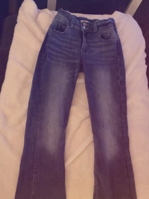 Blå bootcut jeans från gina tricot - Säljer ett par klassiska blå bootcut jeans från gina Young med snygg slitning och broderade bakfickor. Jeansen har normal midja och är tillverkade i mjuk denim som sitter skönt