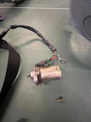 Liten elektrisk motor med kablar - Säljer en liten elektrisk motor i metall med tillhörande kablar, svart och grönt skyddande hölje samt anslutningsögla. Motorn har ett kugghjul i ena änden och passar till olika hobby- eller teknikprojekt.