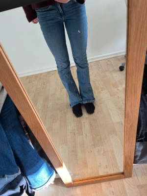 Blå bootcut jeans med låg midja - Säljer ett par klassiska blå bootcut jeans med låg midja och femficksmodell. Jeansen har en snygg tvätt och lätt utsvängda ben. Perfekta till sneakers eller boots och riktigt sköna att bära hela dagen.